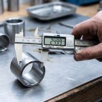Digital calipers measuring the inside diameter of a hardened steel sleeve bushing to choose an exact replacement