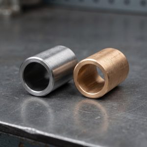 Hardened steel sleeve bushing and bronze bushing side by side for a heavy equipment pin joint comparison